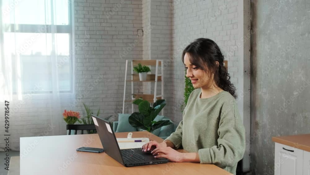 Beautiful young woman working using laptop, raising her hands up in joy, passed an important test. Home office in the kitchen. Beautiful young woman working using laptop, raising her hands up in joy, passed an important test. Home office in the kitchen.