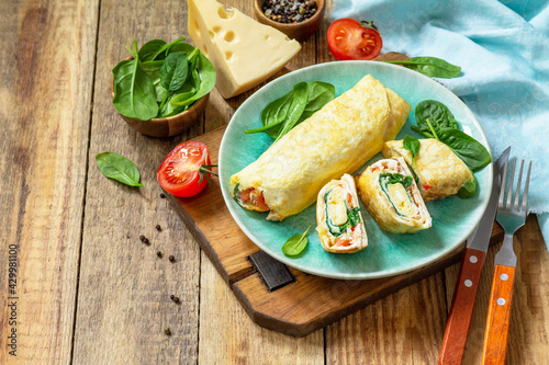 Japanese cuisine. National Japanese dish Omelet tamago yaki for breakfast. Rolled egg with spinach, tomato and cheese on a wooden table. Copy space.