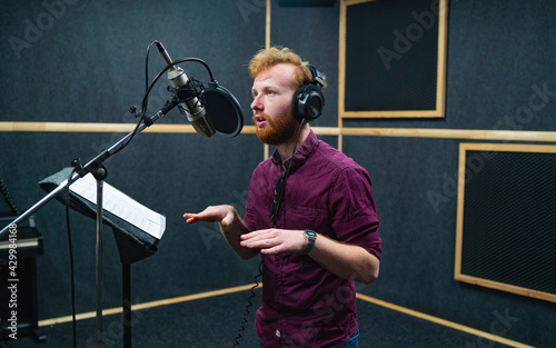 Obraz na plátně Expressive bearded man with curly ginger hair in headphones at recording studio