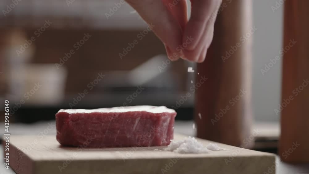 Slow motion slide shot of man seasoning raw beef steak resting on oak board closeup Slow motion slide shot of man seasoning raw beef steak resting on oak board closeup