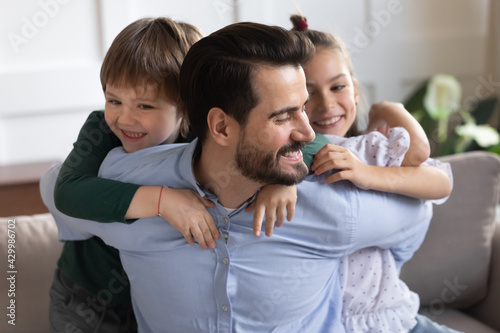 Overjoyed loving young Caucasian father have fun engaged in funny game activity with two small children at home. Happy dad parent and little kids play together, relax on family weekend indoors.