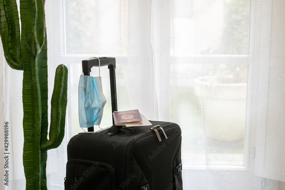Fototapeta premium Luggage trolley bag ready to a new travel during covid-19 quarantine. Business travel flying with coronavirus protections. Passport boarding pass and medical mask. Safety travel, virus health concept