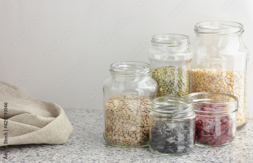 Variety of dry legumes: kidney bean, peas, green gram in glass jars uncooked on white kitchen background, zero waste, eco friendly, balanced diet food, healthy clean eating, vegan protein concept Variety of dry legumes: kidney bean, peas, green gram in glass jars uncooked on white kitchen background, zero waste, eco friendly, balanced diet food, healthy clean eating, vegan protein concept