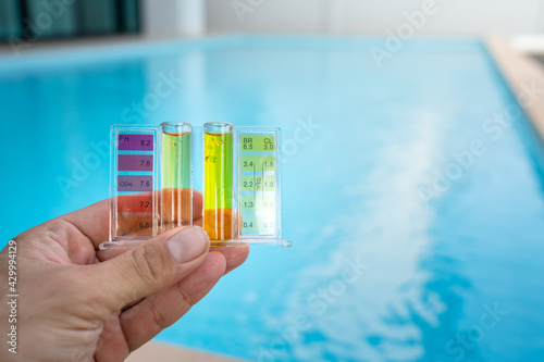 Checking water quality of swimming pool by using chemical test kit to compare PH and chlorine concentration, photo with blurred background of clearly blue water surface. photo