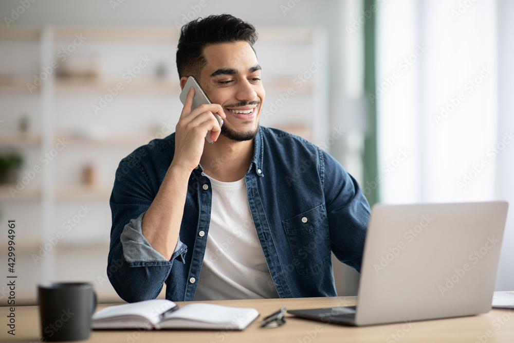 Middle-eastern man working online, using laptop and mobile phone Middle-eastern man working online, using laptop and mobile phone