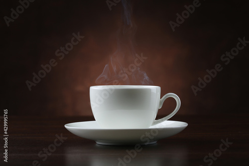 Cup of coffee with steam on brown background