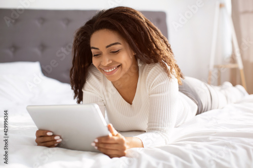 Happy black woman lying in bed using tablet