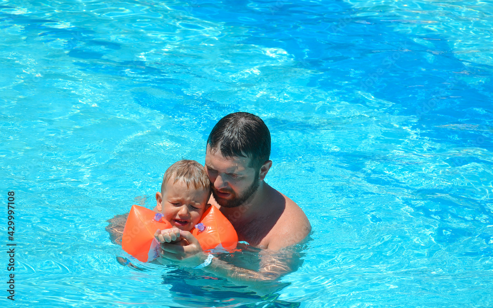 Dad helps his son learn to swim. The child is upset.
