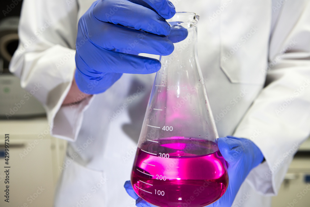 Scientist in a laboratory holding a volumetric flask containing a purple chemical. Titration analysis