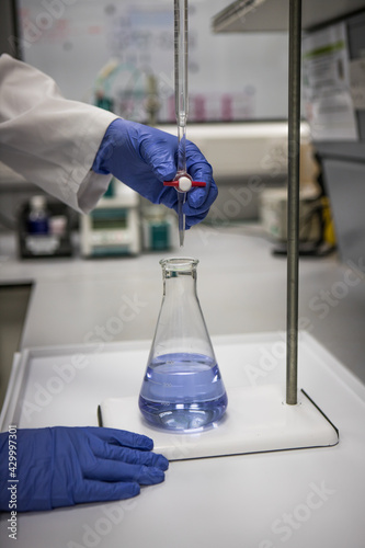 Chemist with gloved hands in a laboratory analysing a sample by titration 