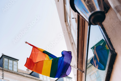Lgbt rainbow flag located on the facade of a building with a old fashioned lamp on it.