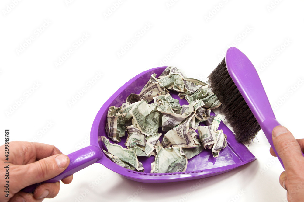 hands hold a dustpan and a broom and sweep up torn, crumpled hundred