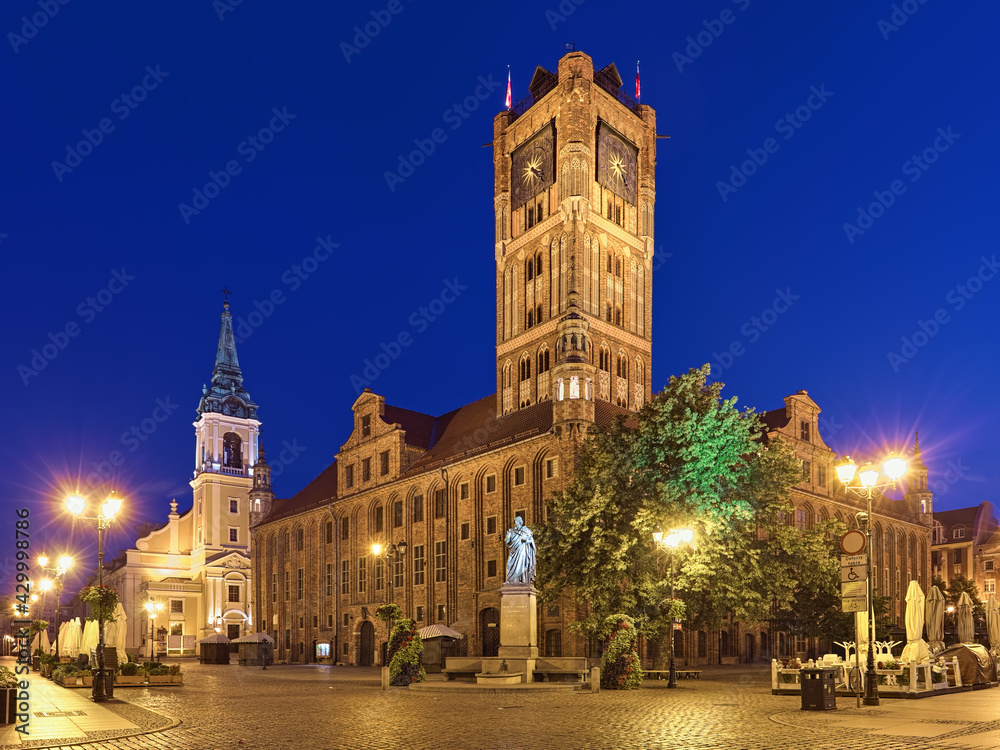 Torun, Poland. Old Town Market Square at dawn with Nicolaus Copernicus Monument in front of the Old Town Hall, and Church of the Holy Spirit in the background. The monument was erected in 1853.