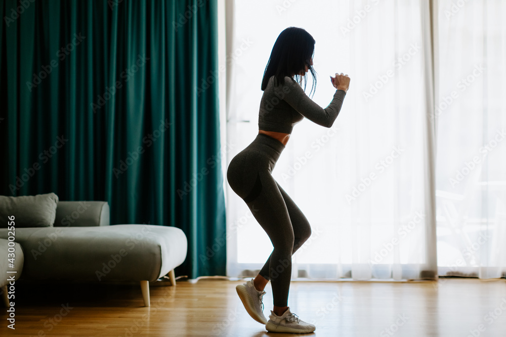 Athletic woman sports workout at home. Home workout. Slim female wearing sports wear stretching at home and weight loss workout in a living room.