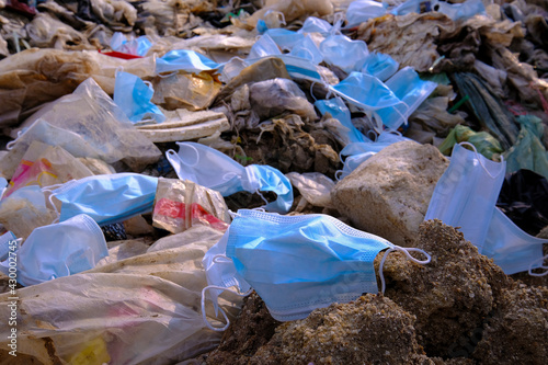 Discarded used medical face masks along and garbage trash with other plastic debris lies on the ground