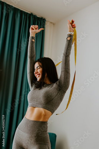 happy Woman Measuring body With Tape after weight loss fitness workout. Beautiful smiling woman measuring butt in front of mirror in living room after fitness marathon