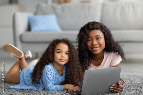 Remote schooling concept. Happy black mother helping her little daughter with online home assignment on laptop, indoors