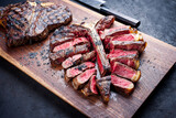 Modern style traditional barbecue dry aged wagyu porterhouse beef steak bistecca alla Fiorentina sliced and served as close-up on a wooden design board