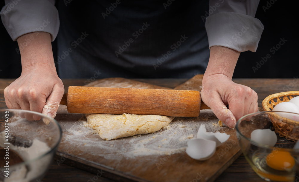 Women's hands, flour and dough. A woman in an apron cooking dough for homemade baking, a rustic home cozy atmosphere, a dark background with unusual lighting. Women's hands, flour and dough. A woman in an apron cooking dough for homemade baking, a rustic home cozy atmosphere, a dark background with unusual lighting.