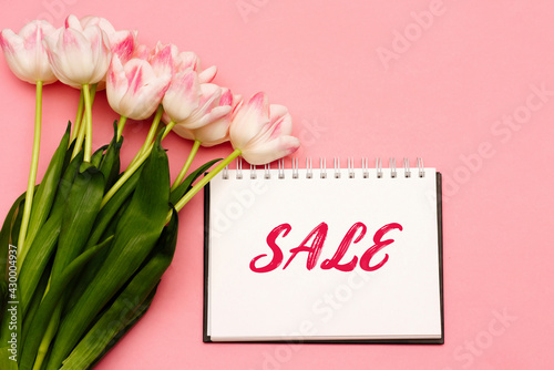 Text SALE next to a beautiful bouquet of delicate pink tulips on a pink background. There may be your text.