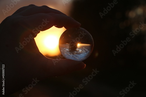 sunset in a beautiful landscape view through a glass ball held by one hand