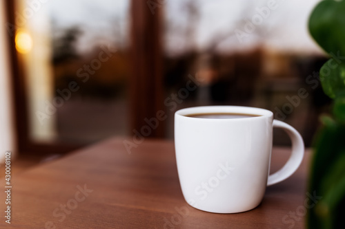 Cup of coffee or tea on the table on the wooden brown terrace during sunset