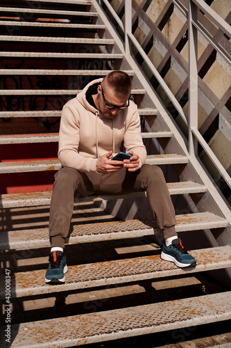 A young man sits on the steps in the city. Urban style. Lifestyle photo