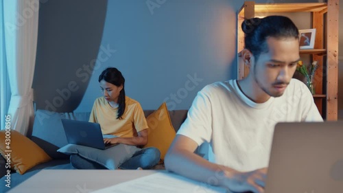 Freelance asia couple man and woman in casual feel serious focus on work separate laptop computer at night, hasband sit in front on table wife sit behind on couch at house. Work from home concept. photo