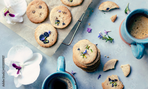 Homemade cookies with edible flowers and mugs of coffee. Helathy food on a spring table. Sweet dessert. Breakfast and freshly baked. Close up and top view.