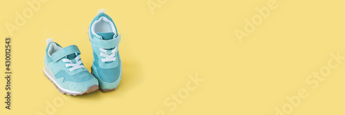 Green sneakers on yellow pastel background. Minimal banner. Concept for sports and physical activity for children and young people.