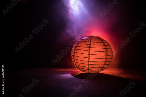 Beautiful paper lantern glowing on wooden table in dark. © zef art