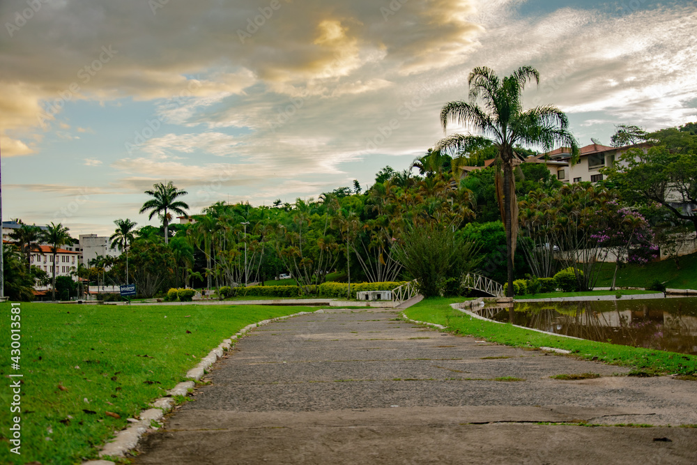Adhemar de Barros square in the center of Aguas de Lindoia with a path for walking and vegetation with trees and palm trees and a lake with the blue sky and some clouds