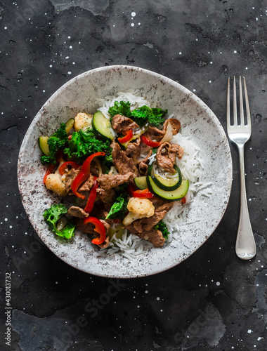 Stir fry beef with zucchini, cauliflower, sweet pepper, kale and rice on a dark background, top view. Asian style food