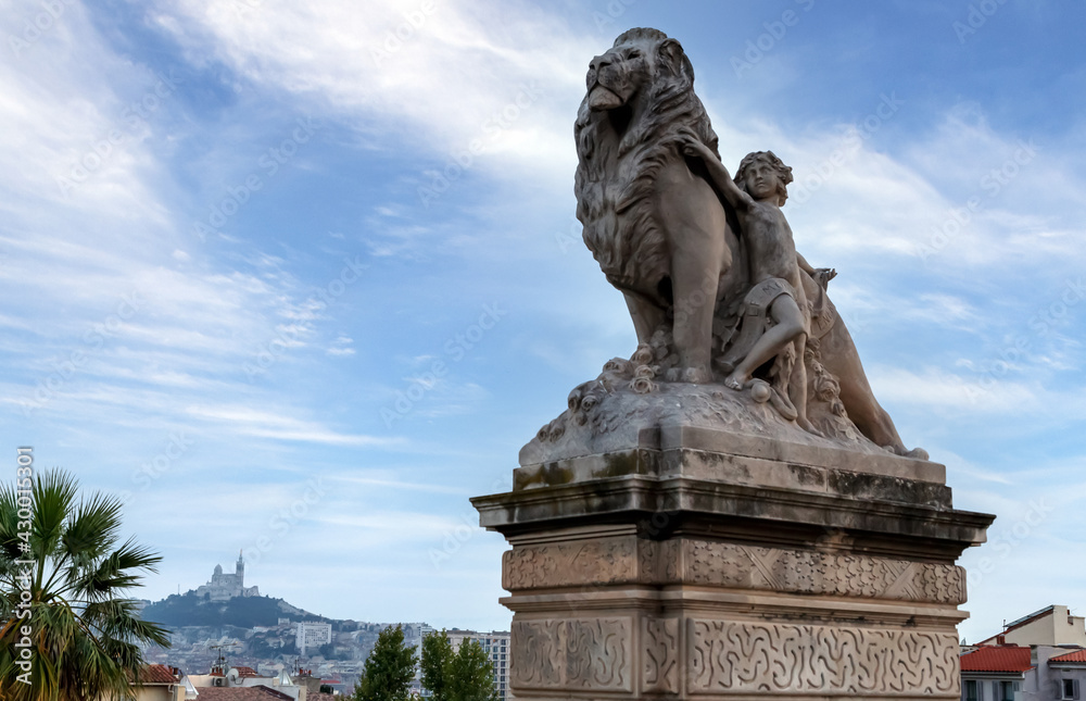 A statue of the lion and child, historical monument in front of Saint-Charles station in Marseille, Notre-Dame de la Garde basilica in the background. Marseille, France.