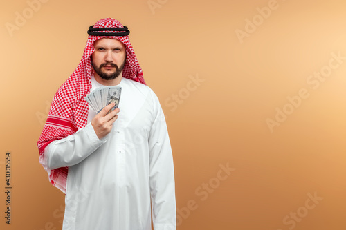 Obraz na plátně Arab man businessman in national clothes is holding dollars in his hands