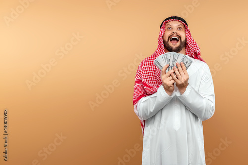 Fényképezés Arab man businessman in national clothes rejoices in dollars in his hands, great profit