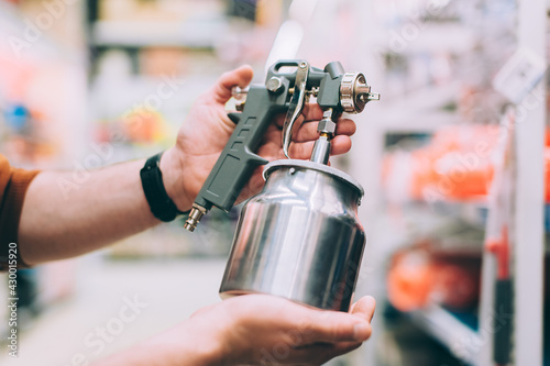 A man in a hardware store holds a spray gun for painting a car.
