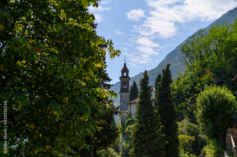 Church seen through green trees full of leaves, blue sky and mountains in background Church seen through green trees full of leaves, blue sky and mountains in background