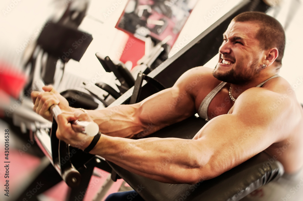 Bodybuilding workout in gym. Powerful muscular man exercising biceps with full power on Scott's bench. Extreme expression in his face. Bodybuilding workout in gym. Powerful muscular man exercising biceps with full power on Scott's bench. Extreme expression in his face.