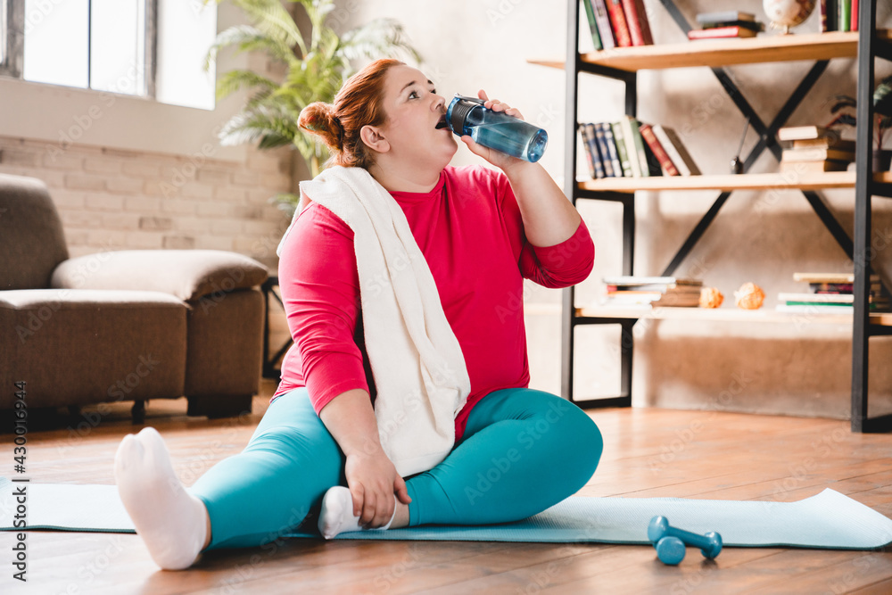 Tired after hard physical training caucasian fat young woman thirsty relaxing on the mat. Chubby plus size woman doing fitness for being in good shape and lose weight Tired after hard physical training caucasian fat young woman thirsty relaxing on the mat. Chubby plus size woman doing fitness for being in good shape and lose weight