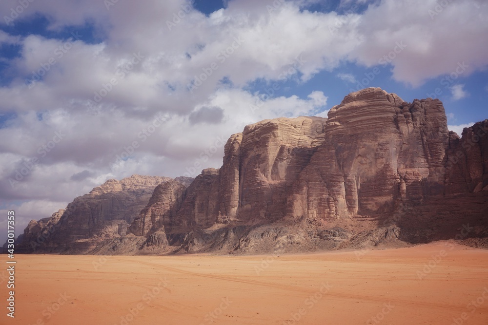 beautiful red relief weathered mountains in the Wadi Rum desert, beautiful white clouds in the blue sky, sunny day, contrasting shadows are on the mountains, nature of Jordan beautiful red relief weathered mountains in the Wadi Rum desert, beautiful white clouds in the blue sky, sunny day, contrasting shadows are on the mountains, nature of Jordan