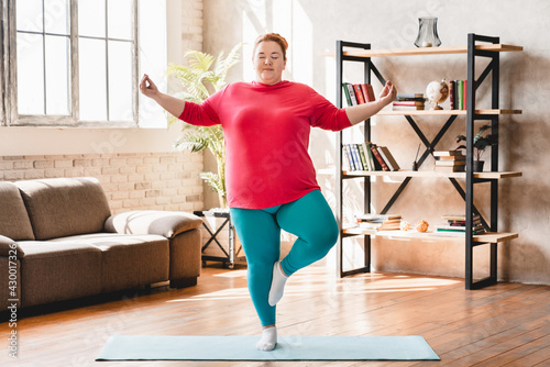 Obese young fat woman standing in yoga position at home. Chubby overweight young caucasian woman practicing fitness for losing weight and burning calories