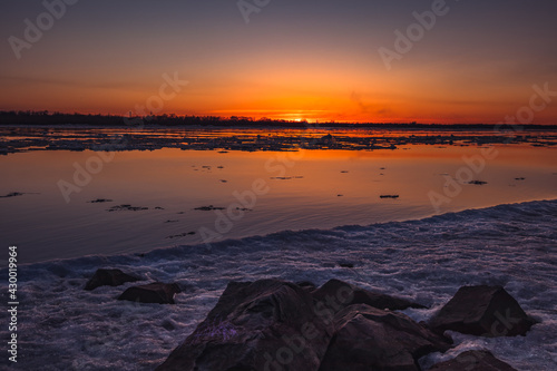 A beautiful sunset over a large river with floating ice and rocks on the shore. Spring season.