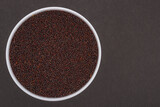 White glass bowl of black mustard seeds. Isolated on a dark grey background.