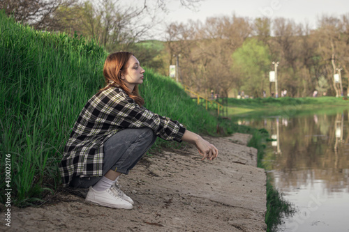 Portrait of a young girl on the background of the lake. The girl is sitting on the shore of the lake. Girl with red hair