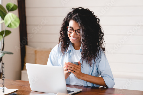 Cheerful relaxed young afro businesswoman having coffee break at work. African girl student elearning distance training course study work at home office. young, watching online education webinar.