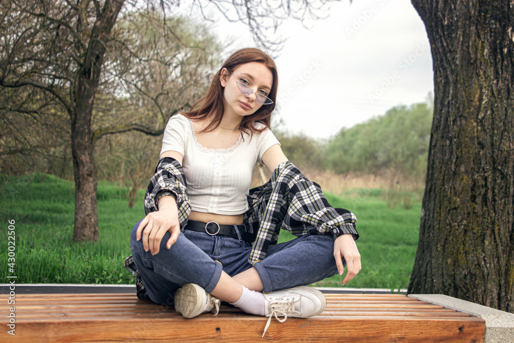 Portrait of a young girl on a background of nature. The girl sits with her feet on a bench in the park. Girl with red hair Portrait of a young girl on a background of nature. The girl sits with her feet on a bench in the park. Girl with red hair
