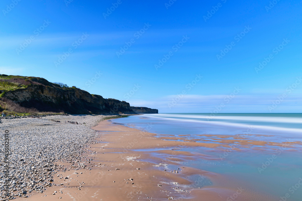 La plage de sable et de galets au pied des falaises de Omaha beach en France, en Normandie, dans le Calvados, au bord de la Manche. - obrazy, fototapety, plakaty 