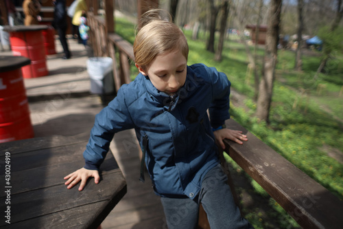 the boy leans his hands on the railing and a wooden table in a cafe in the spring in the park