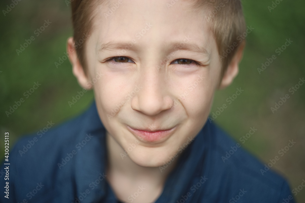 Portrait of a boy on the background of a green lawn. The child makes a face on the camera Portrait of a boy on the background of a green lawn. The child makes a face on the camera
